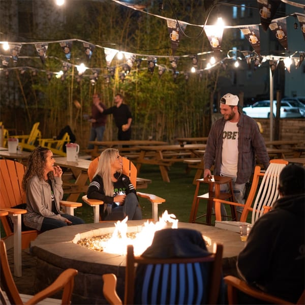 Patrons socialize around a fire pit on the Tennessee Avenue Beer Hall outdoor patio at night.