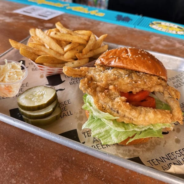 A fried soft-shell crab sandwich with lettuce and tomato, served with fries, coleslaw, and pickles.