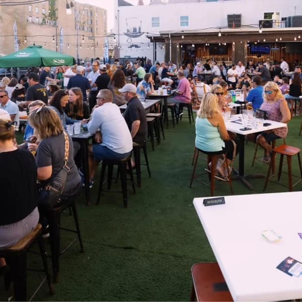A lively outdoor patio at Tennessee Avenue Beer Hall with many people seated at tables on artificial turf.