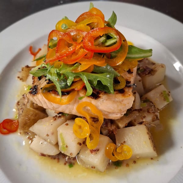 Grilled salmon topped with colorful bell peppers and arugula, served over diced potatoes.