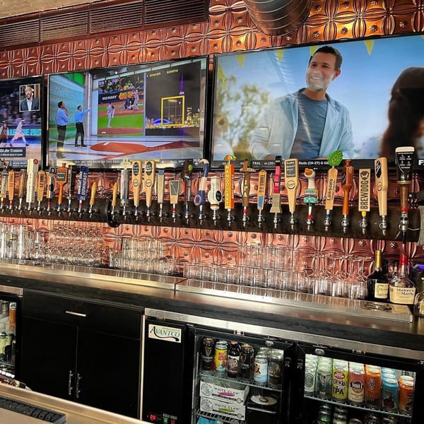 A long bar with many beer taps, glasses, and TVs showing sports, at Tennessee Avenue Beer Hall.
