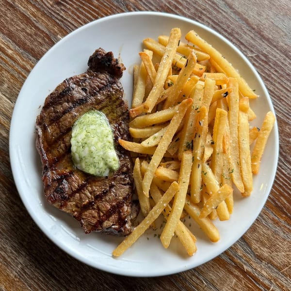 Grilled steak with a dollop of green herb butter and a side of golden french fries.