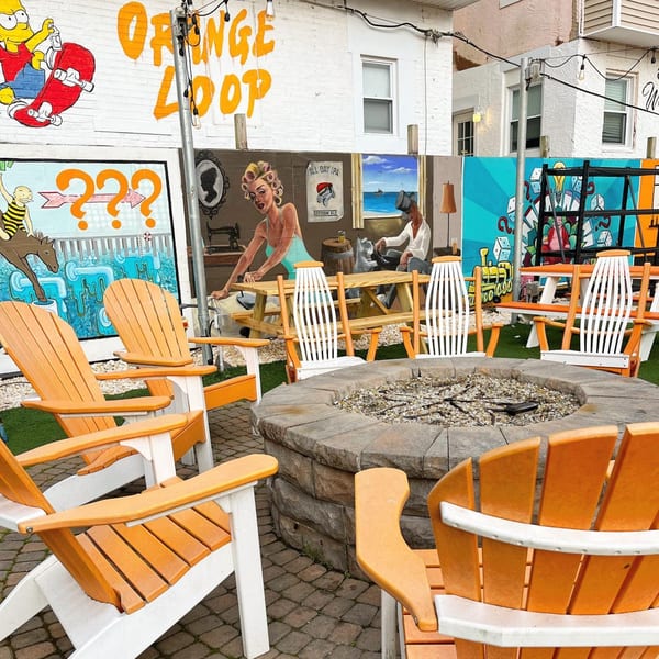 Outdoor seating area with orange Adirondack chairs around a fire pit, surrounded by colorful murals.