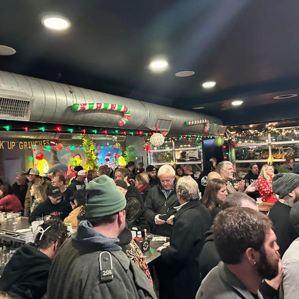 Crowded bar area decorated with Christmas lights and candy canes, filled with many people.