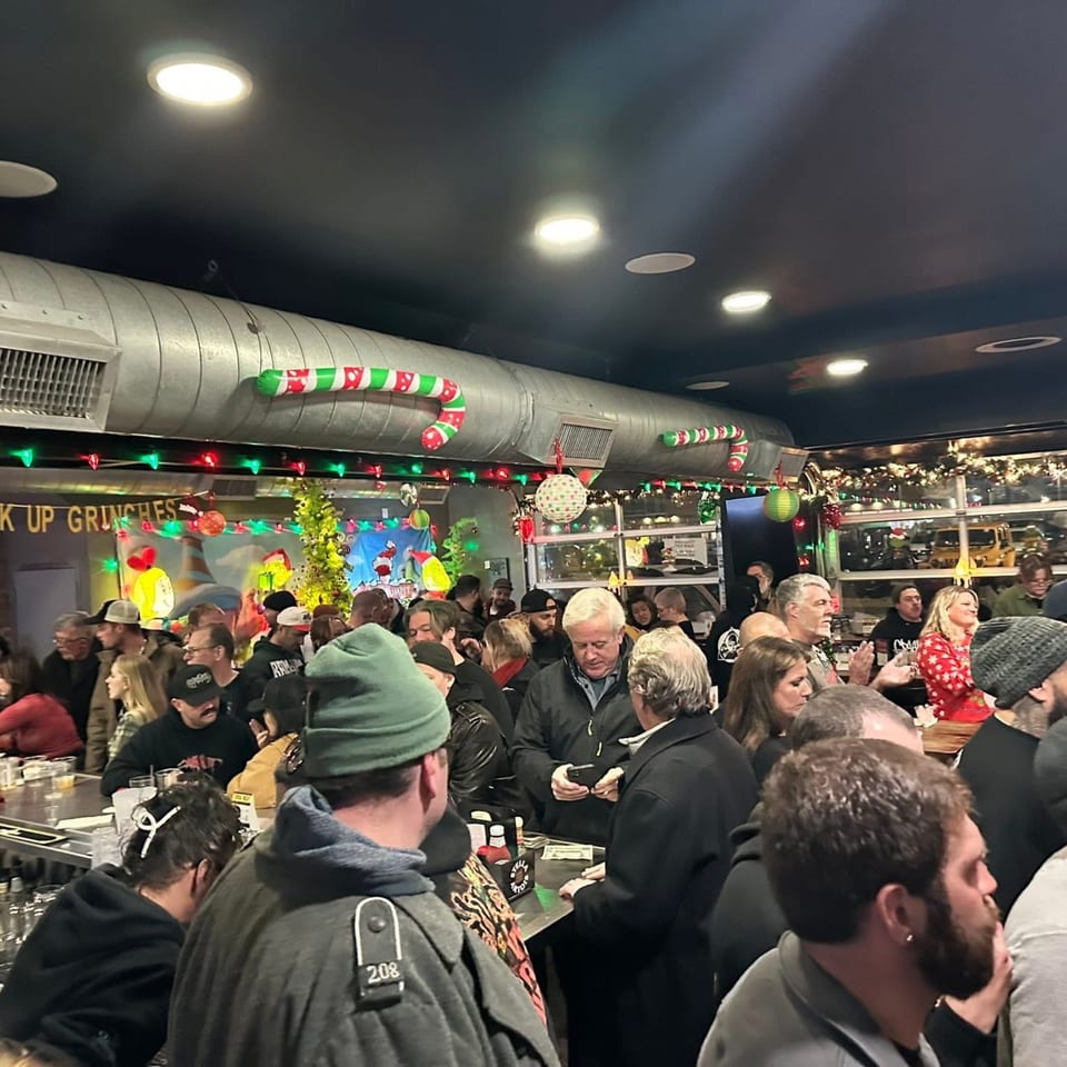 Crowded bar area decorated with Christmas lights and candy canes, filled with many people.