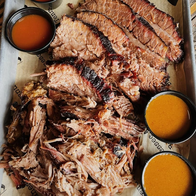 Sliced and pulled brisket with three small cups of barbecue sauce on a metal tray.