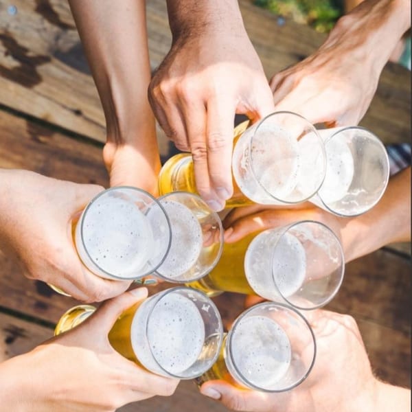 Multiple hands holding beer glasses in a toast, viewed from above, on a wooden surface.